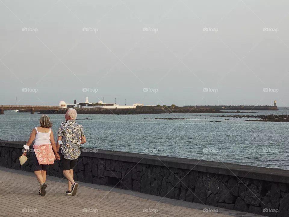 elderly couple strolling on a promenade, overlooking the sea in times of pandemic