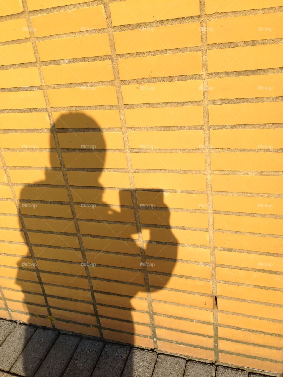 Shadow of me taking a picture of a yellow brick wall.