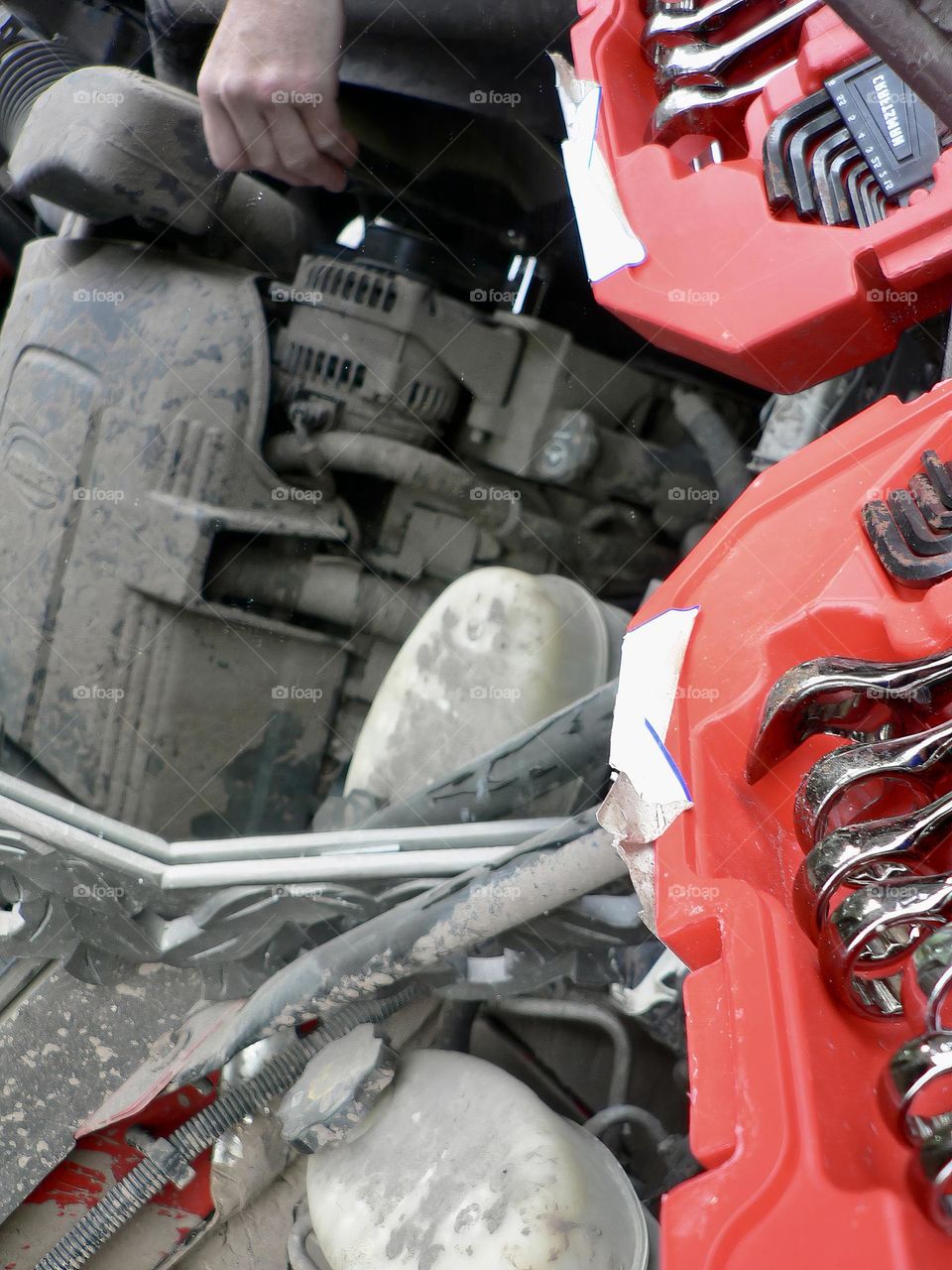 Under the hood of a red pickup truck with combination wrench set tools organized in a red tool hard case by the work station with its reflection from a mirror.