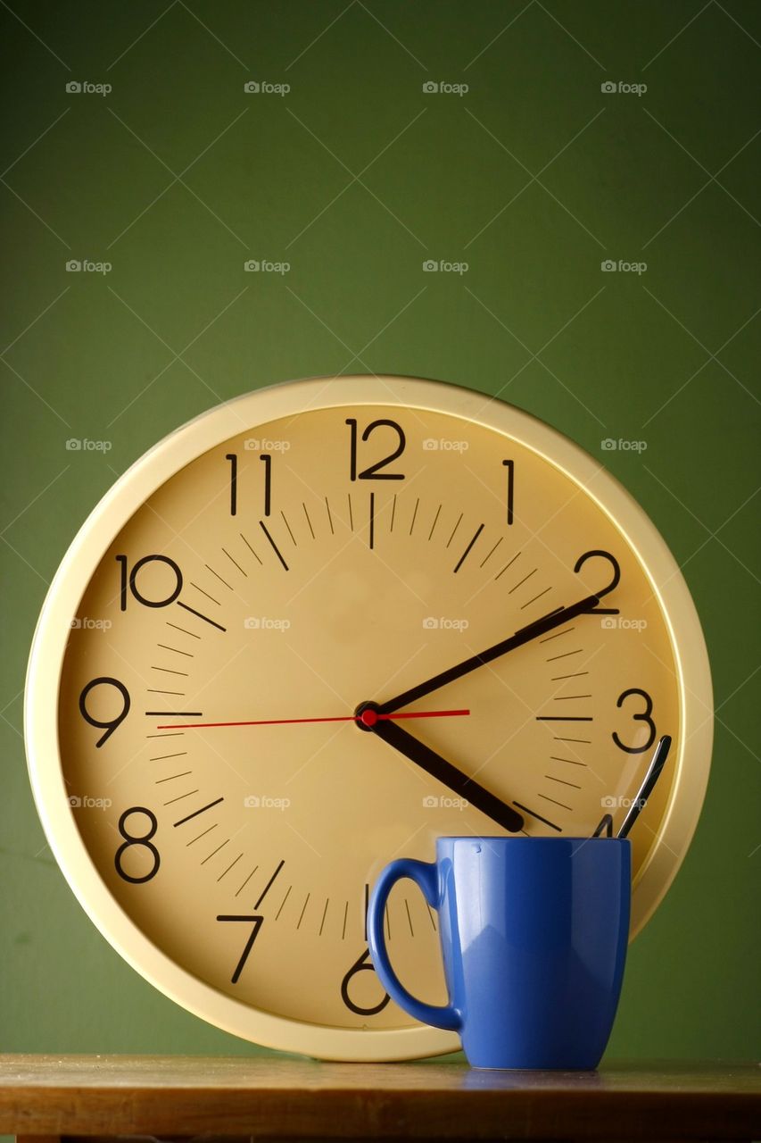 blue coffee mug with teaspoon and an analog clock