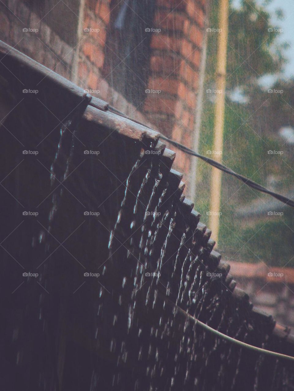 Close-up of rain falling from house roof. Rainwater flows from the edge of the roof which is made of dark, rough material in low angle view