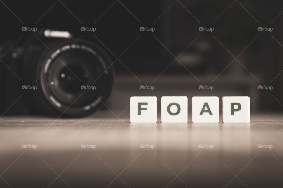 Foap spelled in letters in front of a camera on a wooden table.