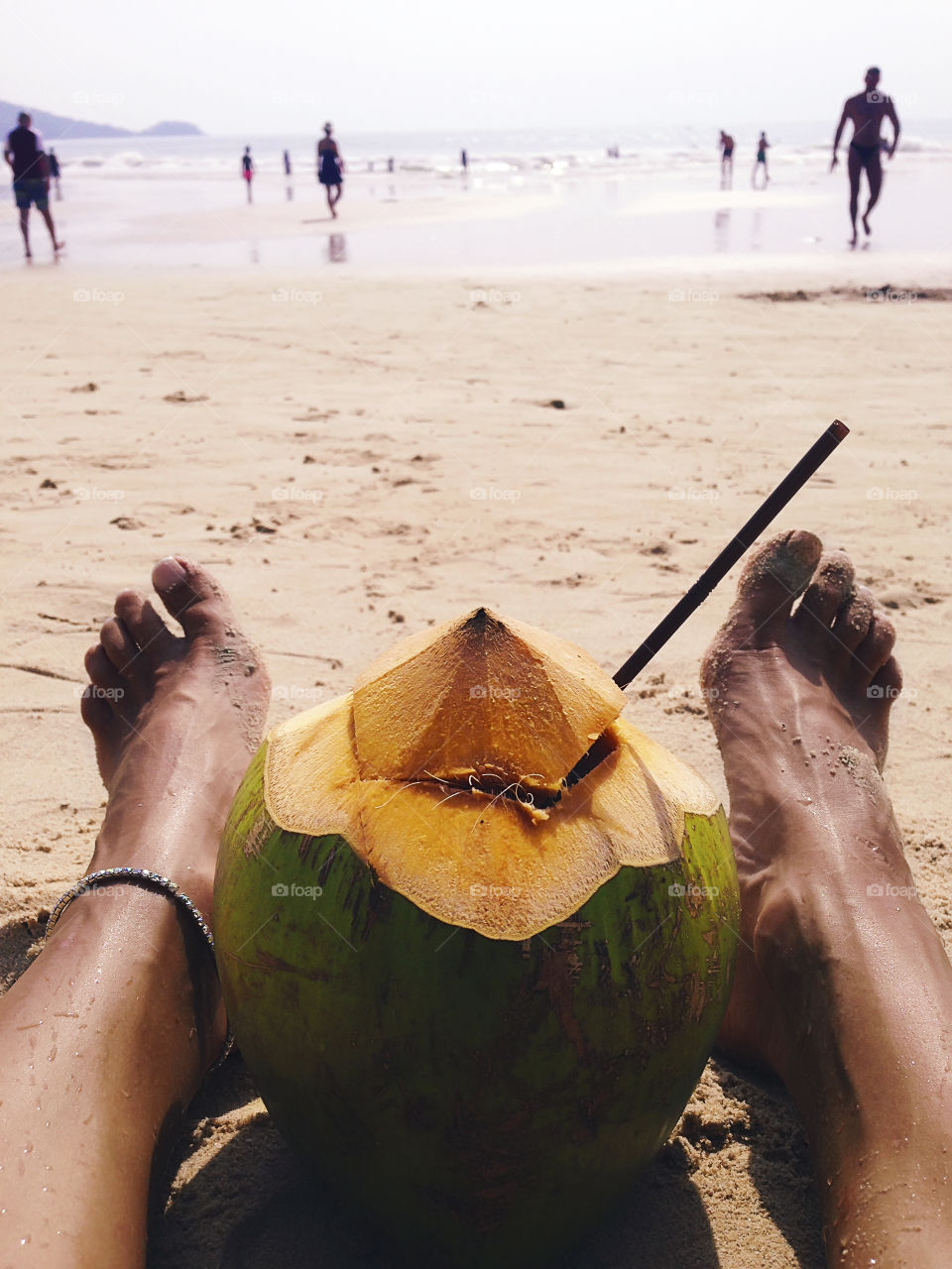 Young woman enjoying her summer tropical vacation at the sandy beach with a coconut cocktail 