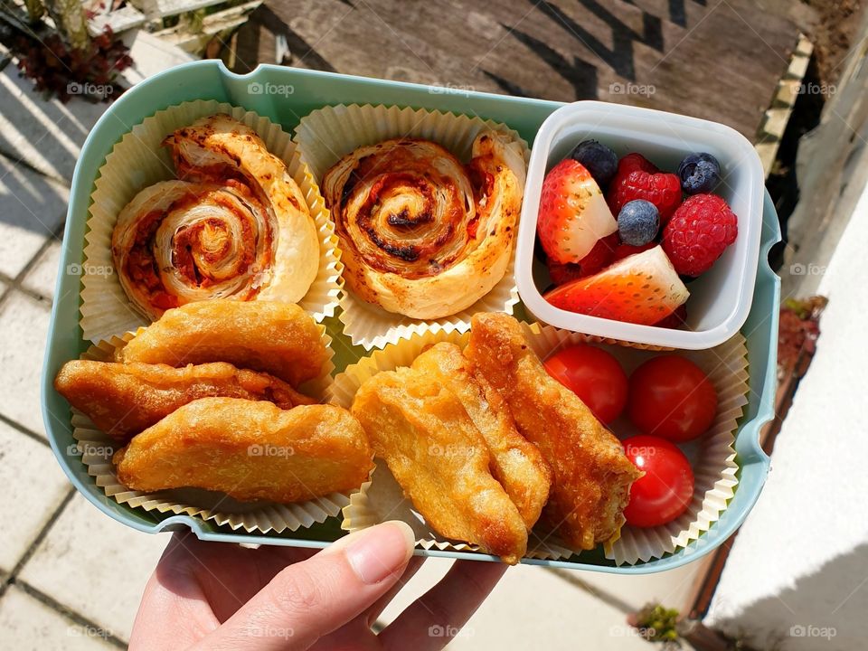 A lunch box filled with pizza rolls, fruit, cherry tomatoes and (vegan) chicken nuggets.