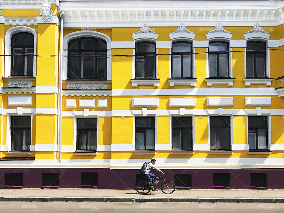 Young man riding a bicycle and using mobile phone in front of the old yellow city building 