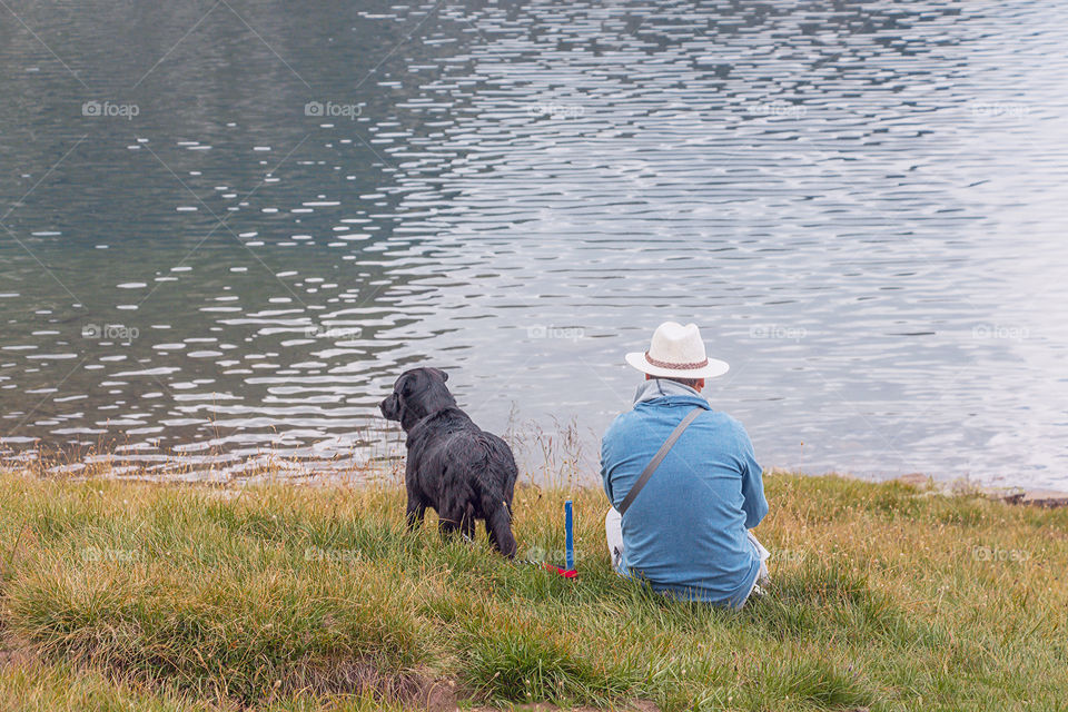 Back side view of dog and its owner watching water and lake and enjoying the view. Picture taken in Rila Mountain - Seven Rila lakes, famous tourist attraction, Bulgaria