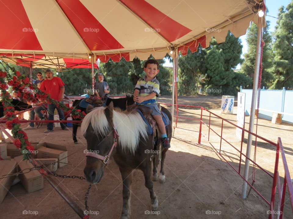 Happy boy riding pony on carousel ride at festival.