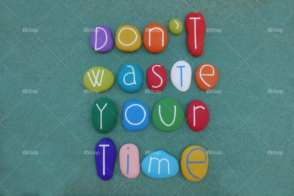 Don't waste your time, motivational words composed with colored stones over green sand