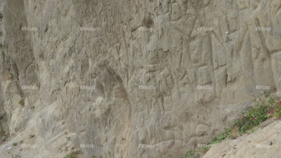 Hearts, symbols, and initials carved into a sandstone cliff face.