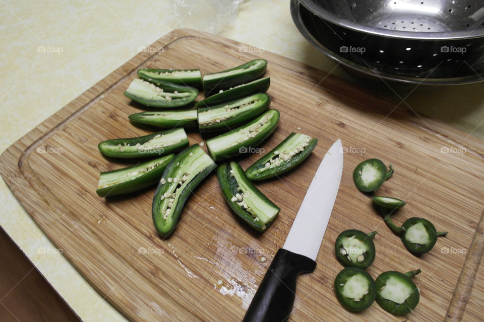 Slicing green jalapeño peppers on a wooden board at home