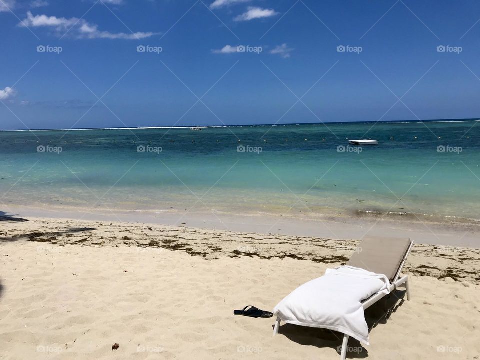 Solo sun lounger on the serene beach in Mauritius. Calming view of blue sky, blue seas and golden sand