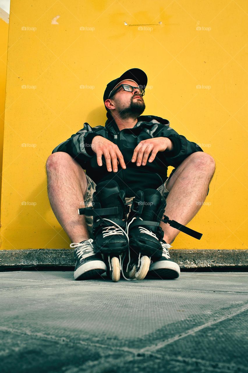 Bearded man with his roller blades sitting by the yellow wall