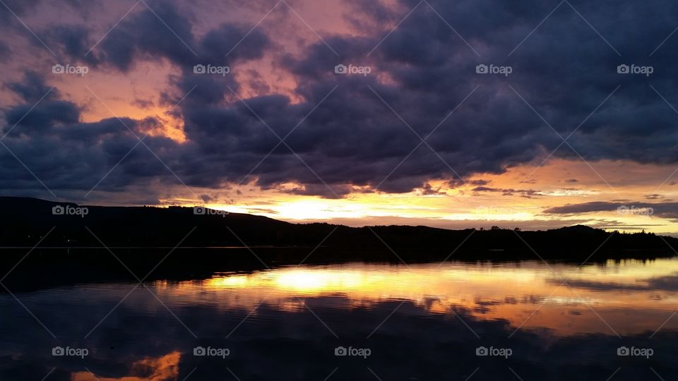very dark Sunset with dramatic clouds reflected in lake