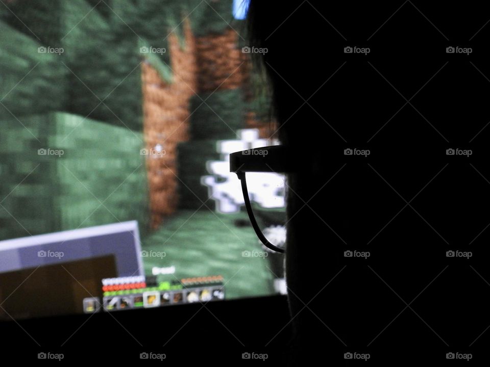 Teenager boy playing Minecraft on the gaming computer seen from his glasses close-up in a dark room.