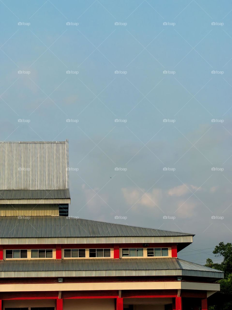 a building with a wavy roof and red and white walls, with a bright blue sky in the background