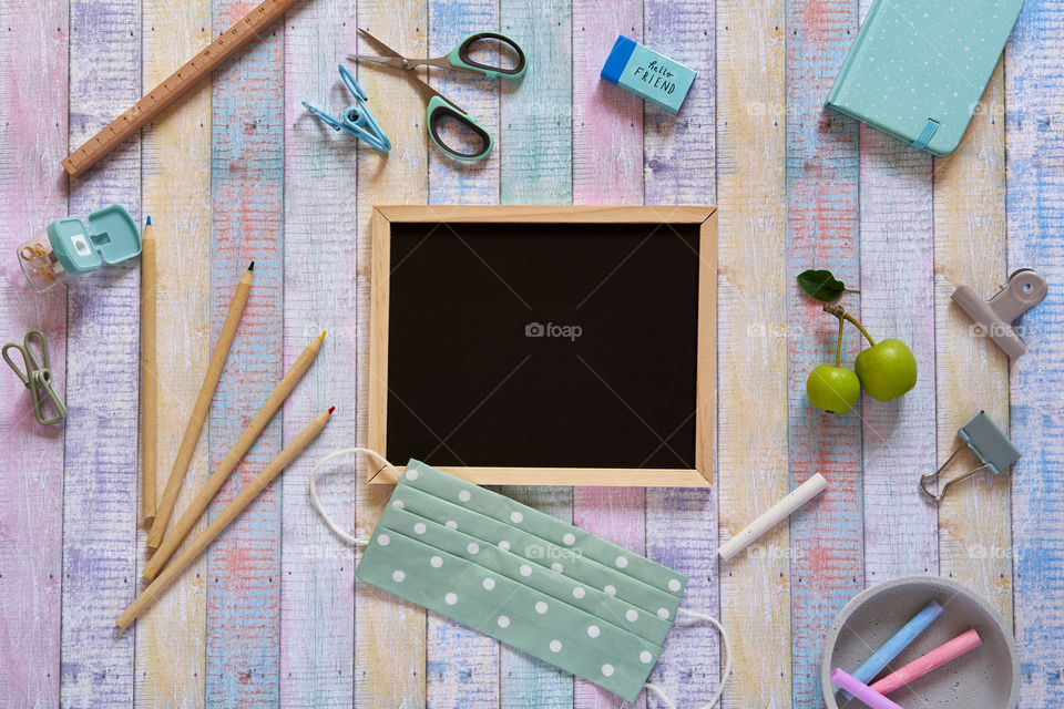 A chalkboard with the school supplies and a safety face mask 