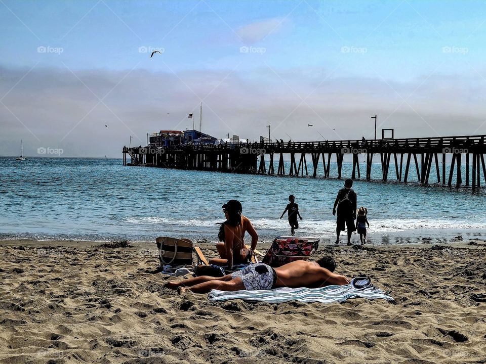 A beautiful sunny day on the beach in Capitola California with the wharf jutting out into the ocean as people relax 