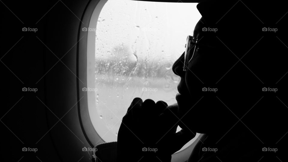 Black and white portrait of a woman wearing a hijab in an airplane window.