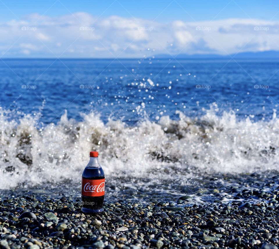 Waves hitting near cola bottle on ocean shore 