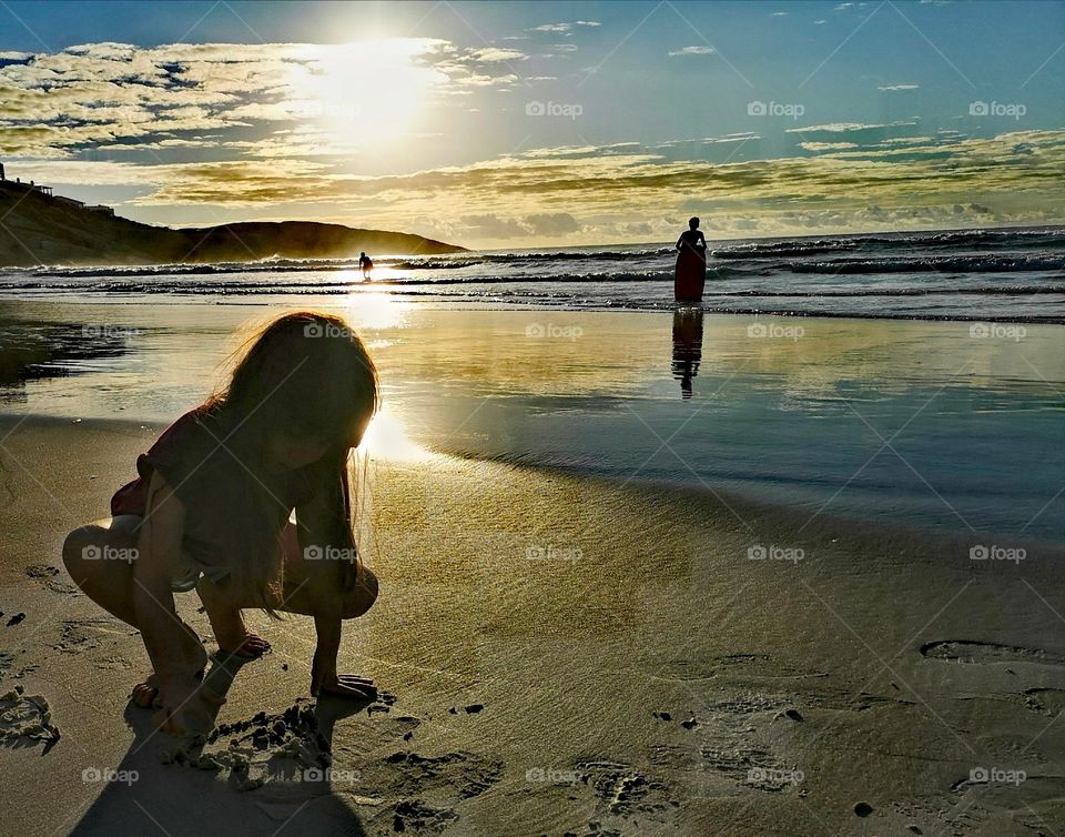 Girl drawing in beach sand at sunset