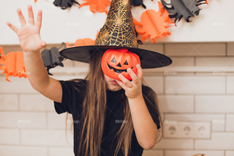 Little girl dressed as a witch for halloween holding a pumpkin with a face on the background decor