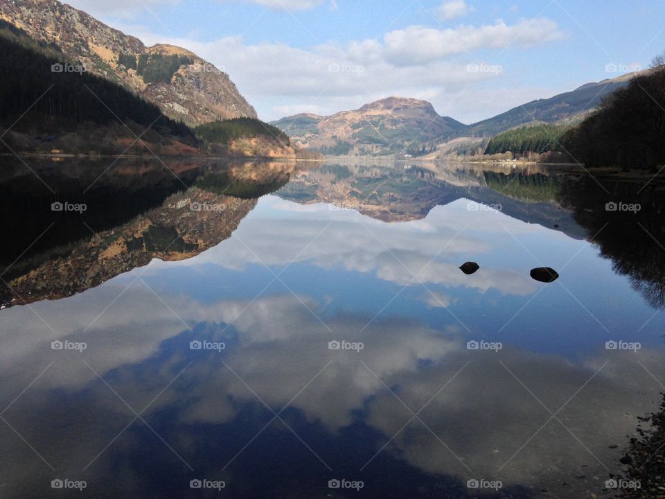A perfect reflection of Scotland's Highland Mountains and cloud-filled sky in a local loch