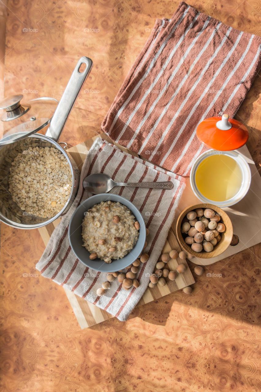 Cooked oatmeal in a deep gray plate with hazelnuts and honey.