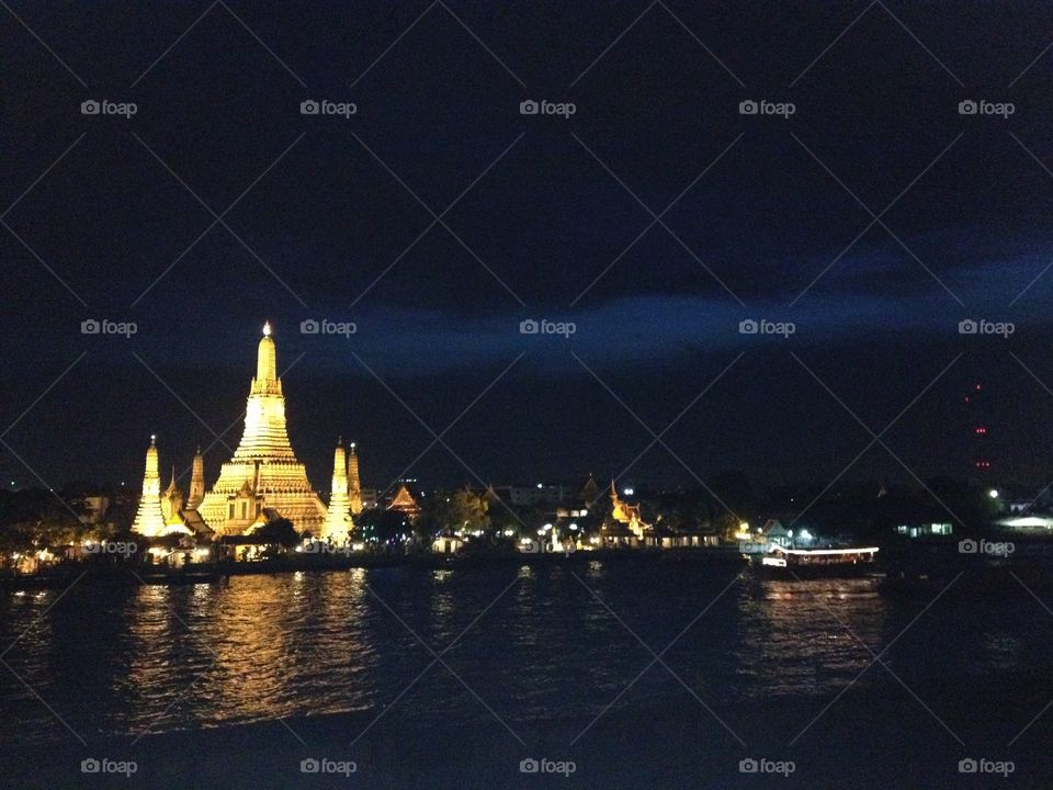 Wat Arun/Temple of Dawn illuminated across the Chao Praya River during the evening in Bangkok, Thailan