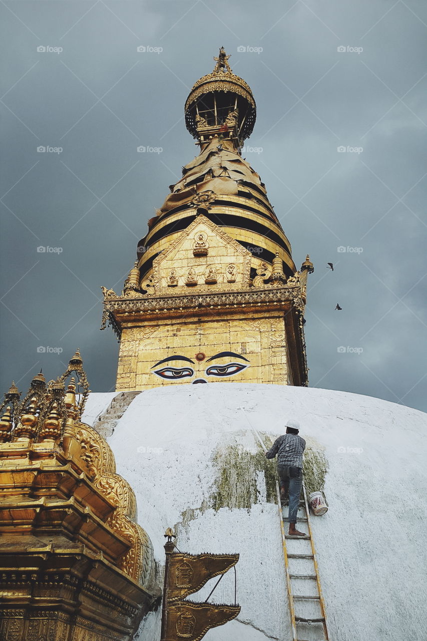 worker paints Buddha stupa. picture was taken at monkey temple. worker paints roof of the temple. it was damaged after Nepal earthquake.