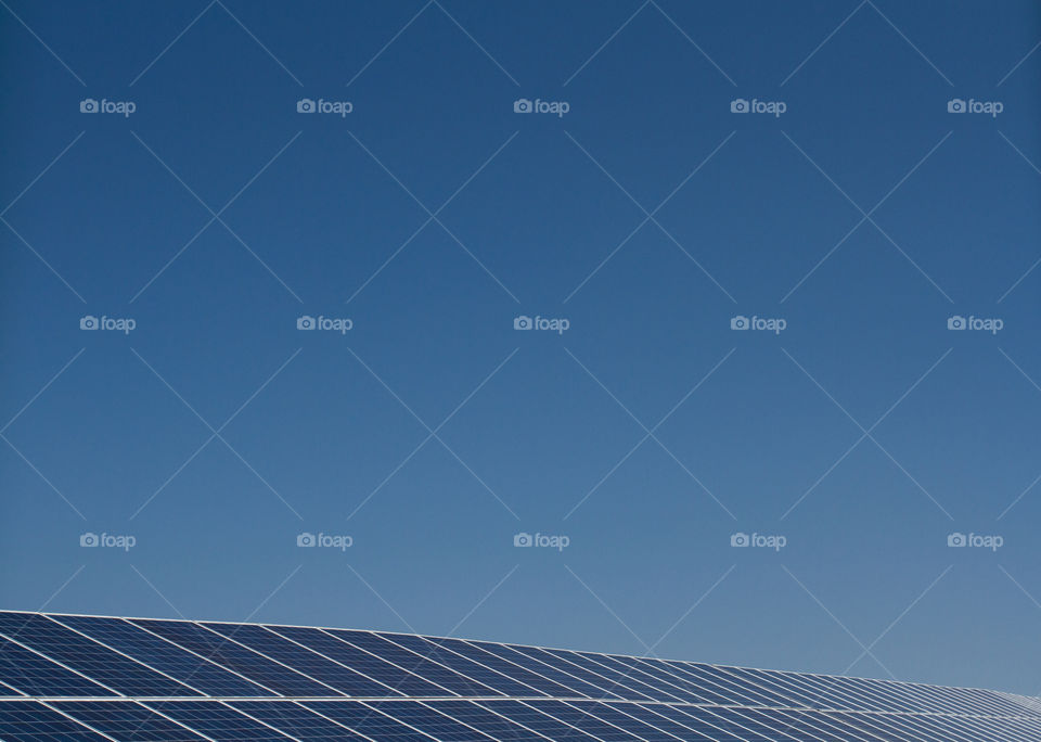 A long row of solar panels generating clean electricity under a clear, blue sky.
