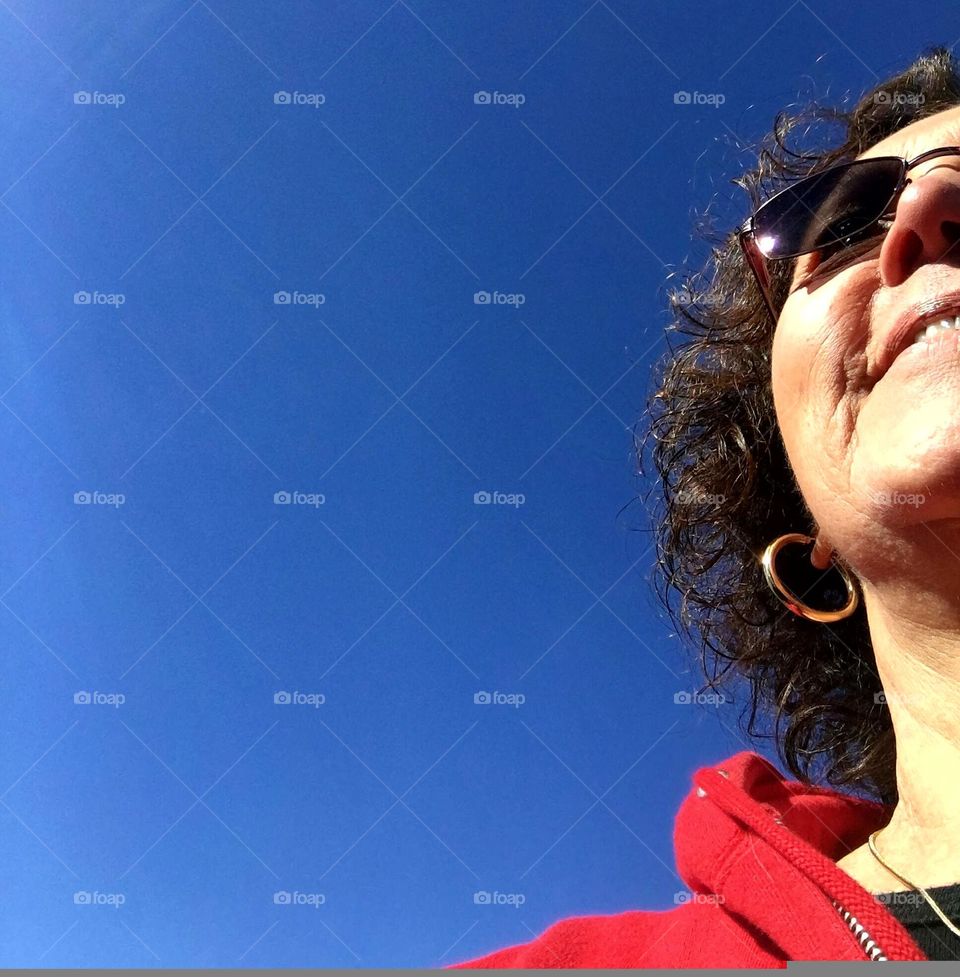 Looking up at the deep blue sky with no clouds. There is a partial view of a womans face that is sun-kissed as she seems happy moving through a beautiful day.