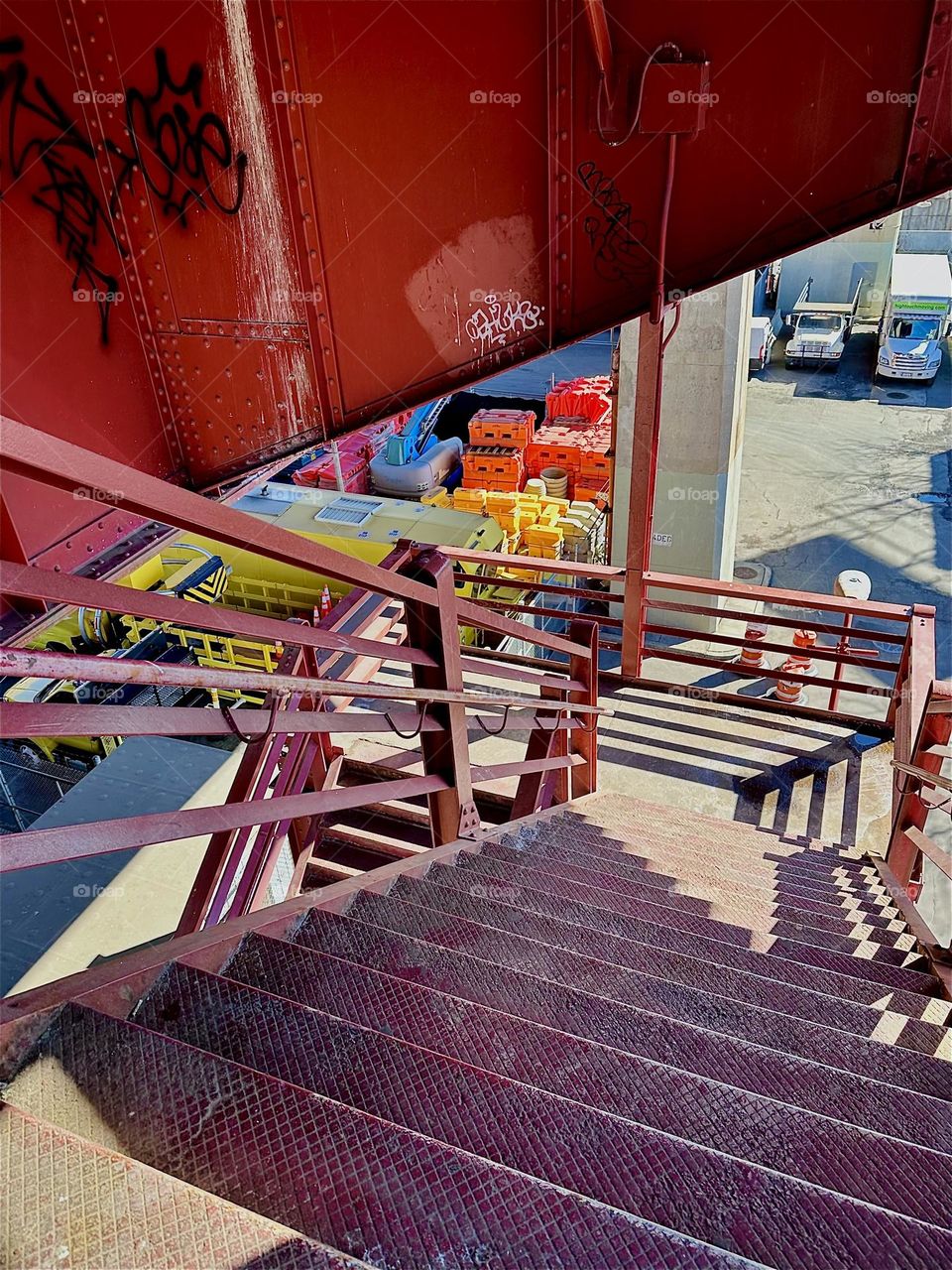 These interesting structures of the red metal staircase and support beams of the “Pulaski Bridge” at “Newtown Creek” in LIC, Queens cast dramatic shadows over the cascading steps downward. 2024. Hypnotic Productions