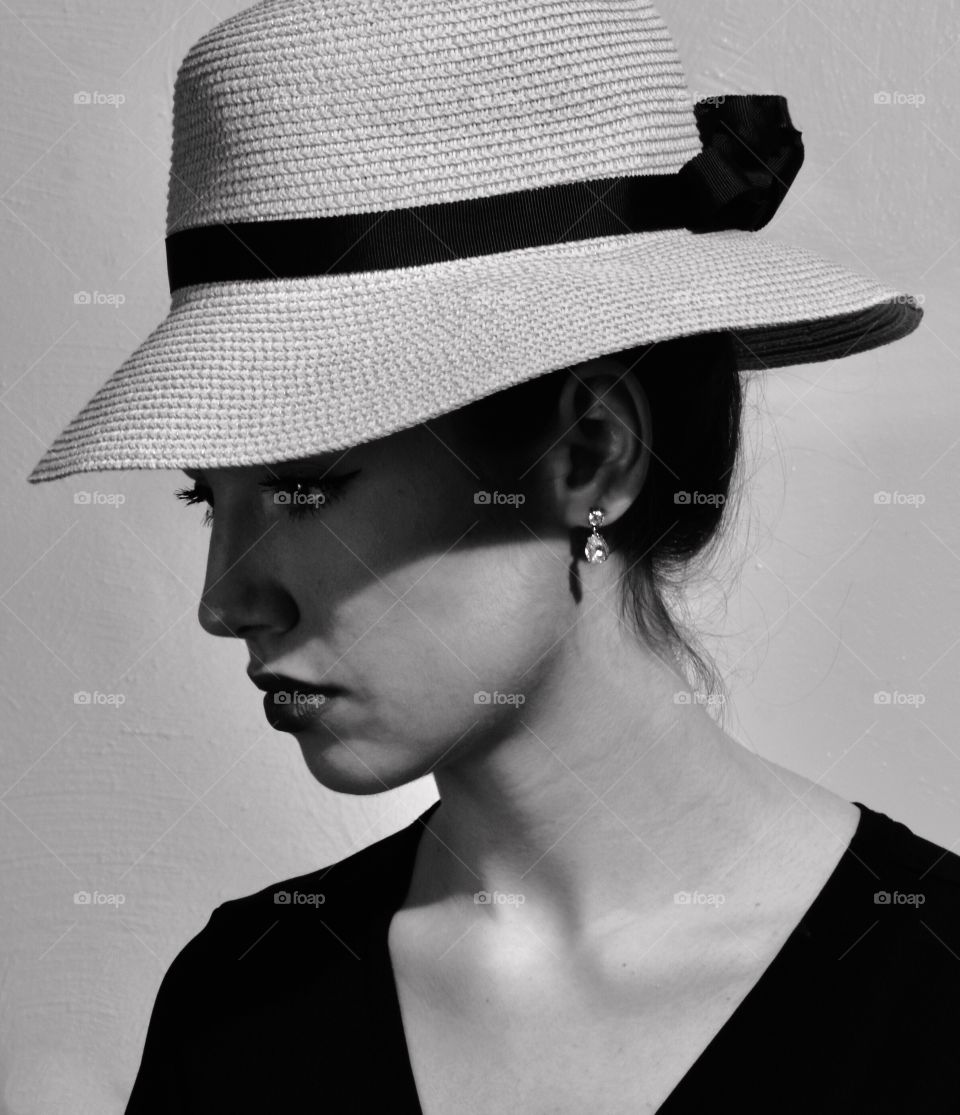 Black and white closeup of a beautiful woman wearing a hat that is shadowing half of her face.