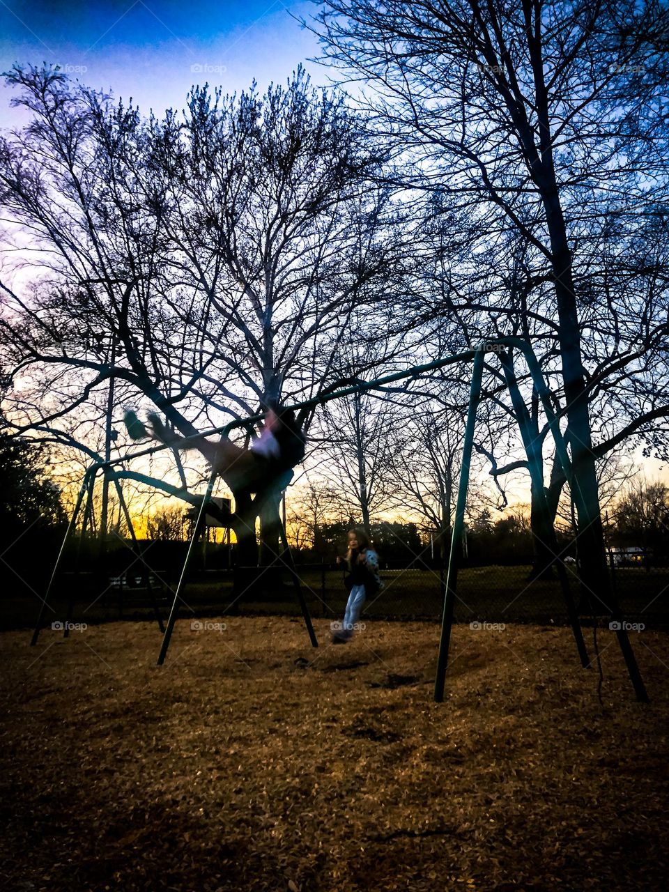 Glowing Sunset evening where Two children swinging in a local park enjoying the wonder of being a kid