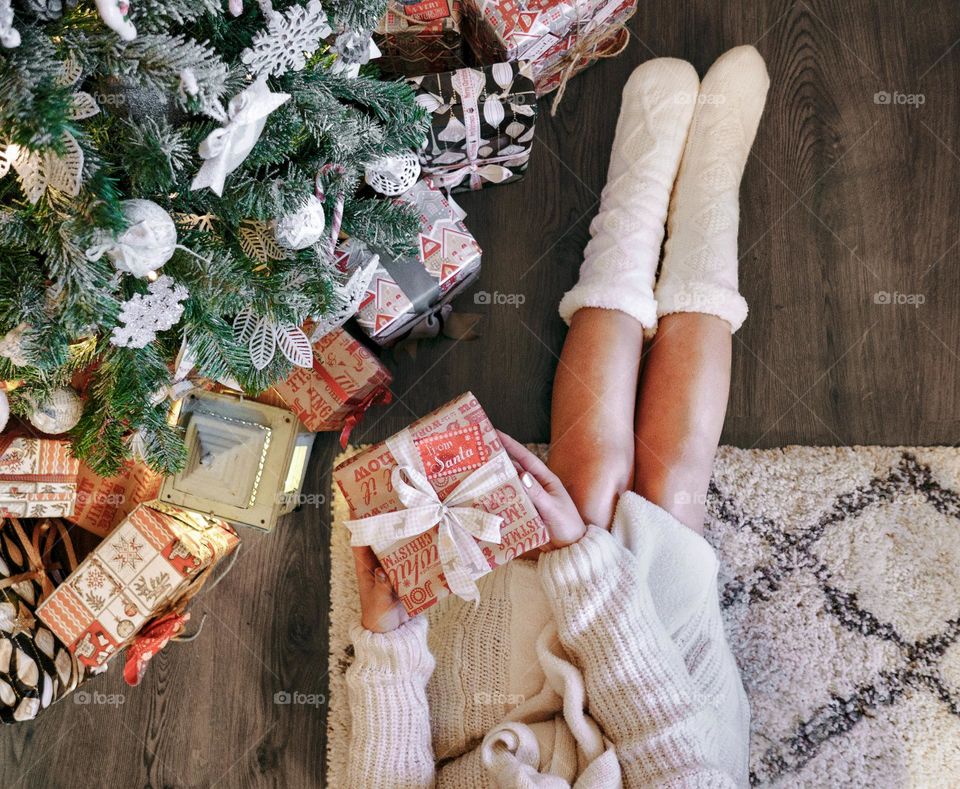 Woman in knitted socks relaxing at a cozy home atmosphere by presents and a Christmas tree