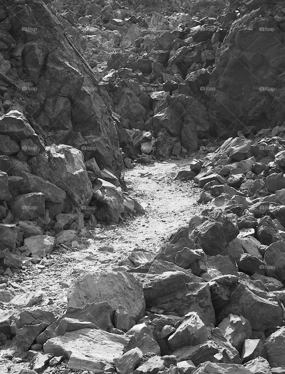 An uphill trail winds through jagged obsidian walls at the Big Obsidian Flow at the Newberry National Volcanic Monument in Central Oregon on a sunny day. 