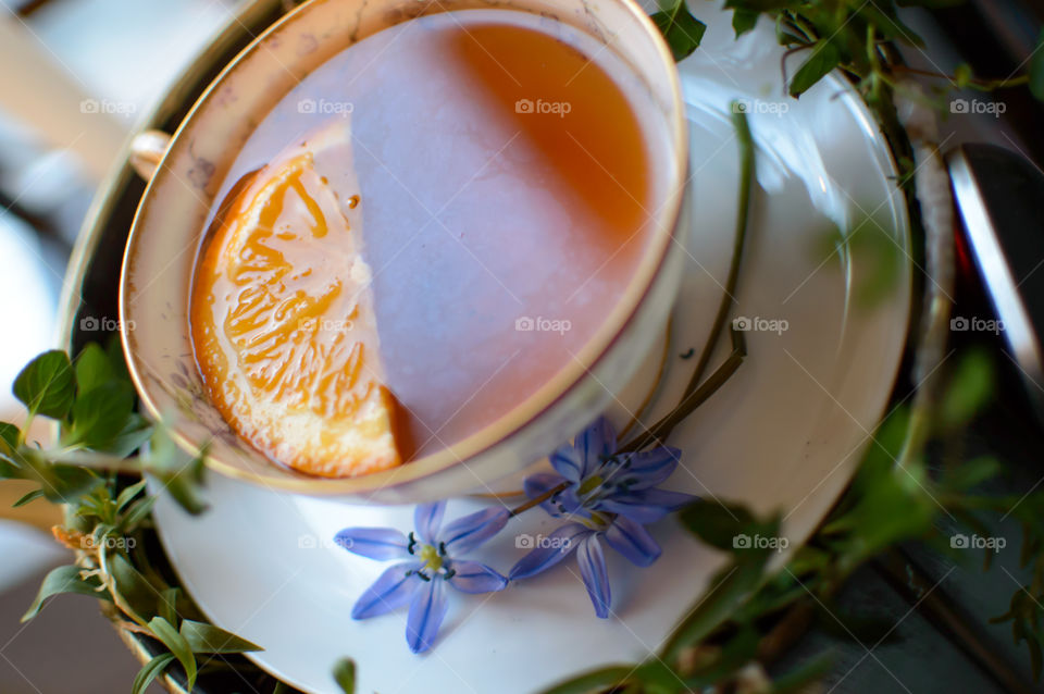 Orange tea with honey in golden hour sun light with fresh lily garden flowers (Scilla siberica) and a wreath of fresh mint leaf 