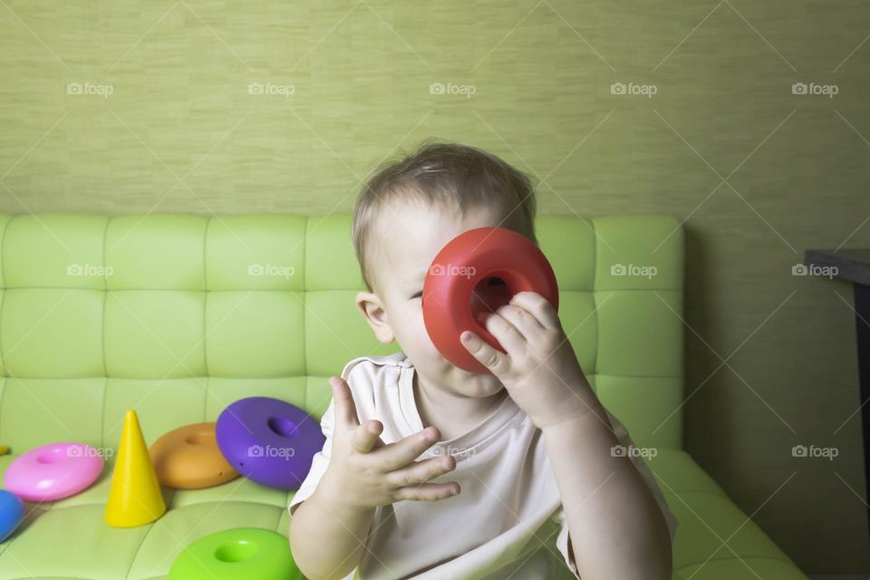 The child is having fun playing a bright pyramid educational toy, sitting on a green sofa.