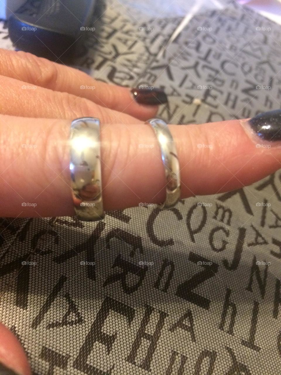 Womans hand, wearing her ex’s 10 carat white gold mens wedding band, and her 24 carat white gold wedding band, both on her manicured gel nail painted blue, pointer finger because they got divorced