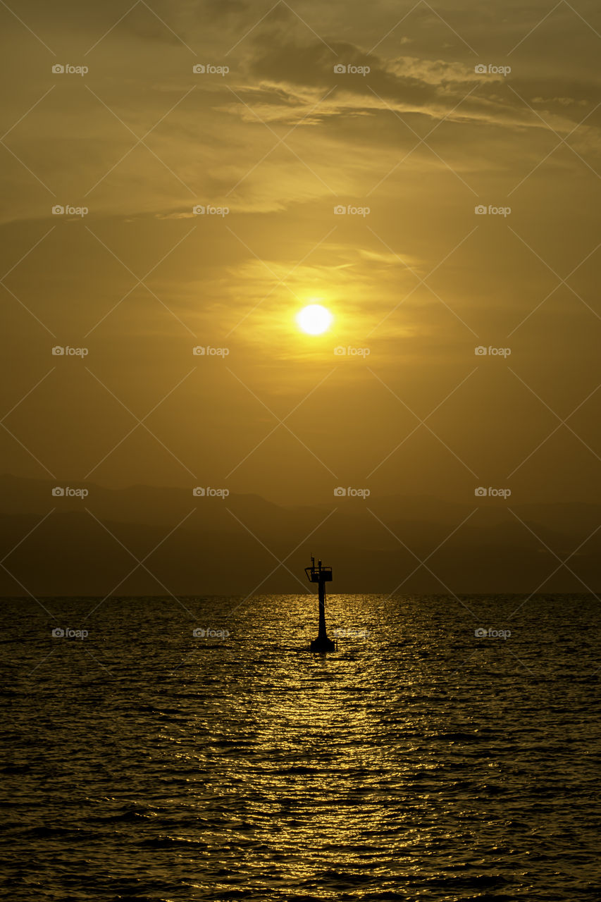 Golden light of sunrise behind the mountains and the shadow of signal lamp for sailing in the sea.