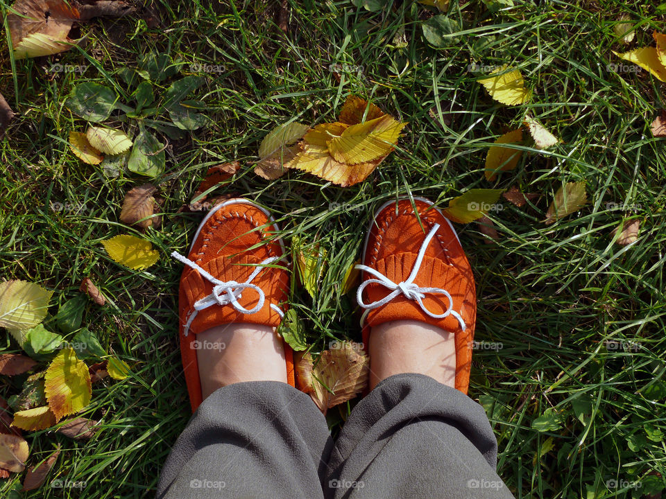 Low section of woman wearing shoes standing by autumn leaves on grassy field.