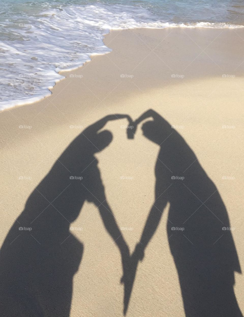 Couple making a heart shadow on the beach with hands, LGBTQ couple on the beach, seaside vacations with LGBTQ couple, expressing their love for one another 