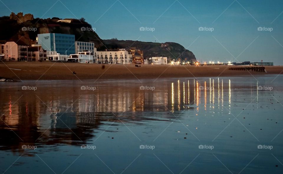 Early evening looking inwards to Hastings seafront and castle on the hill,  with the town lights reflected of the wet beach