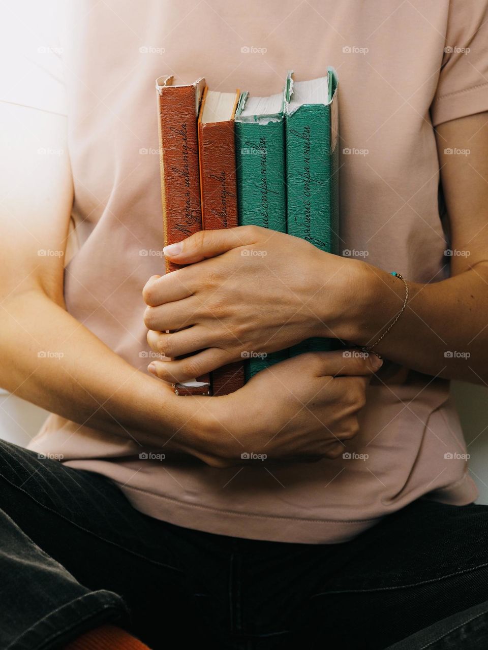 Unrecognisable woman in pink T-shirt holding a stack of books in the library 