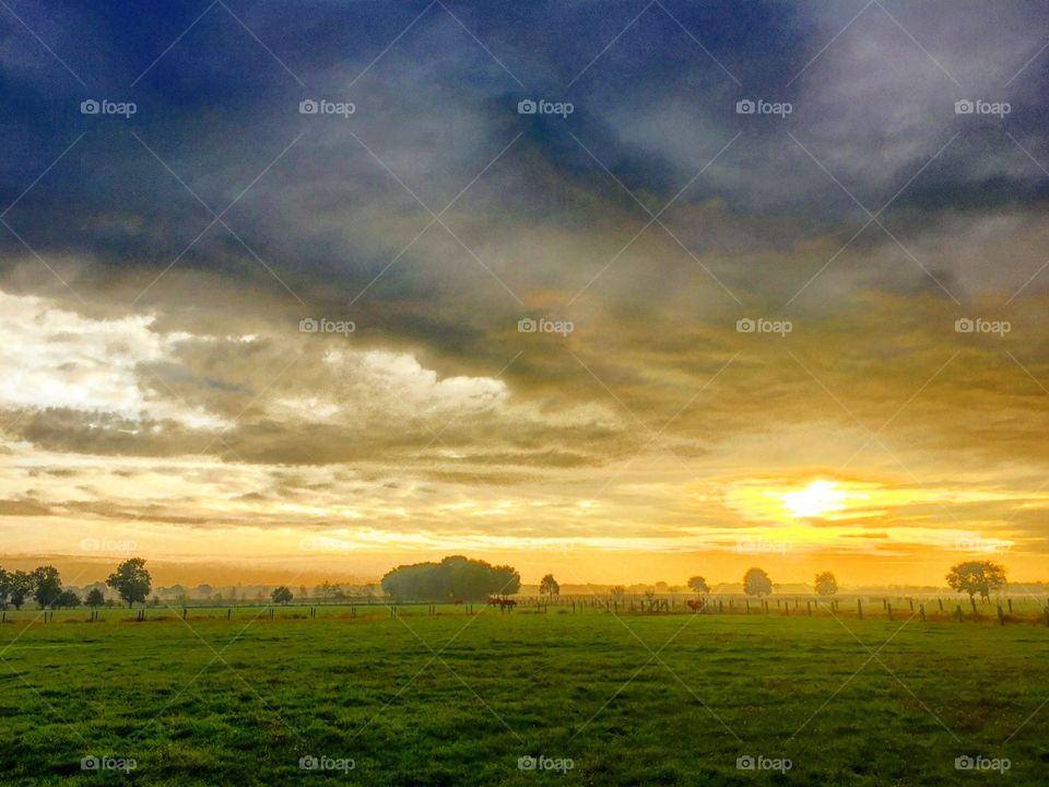 Stormy rainy clouds darkening the sky with a sunrise underneath over a rural Countryside landscape 