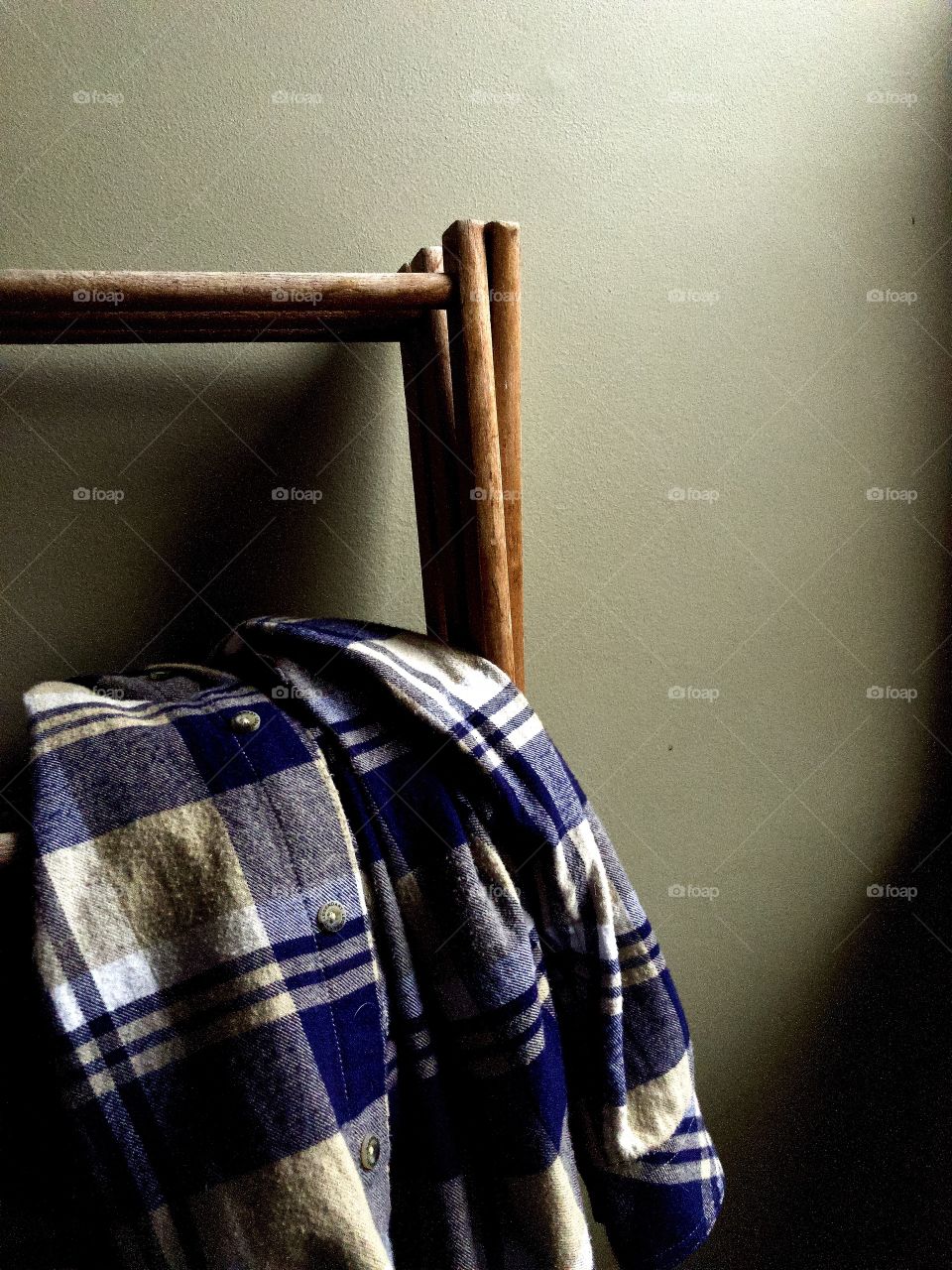 Men’s plaid flannel shirt folded over wooden clothes rack in soft light and shadow