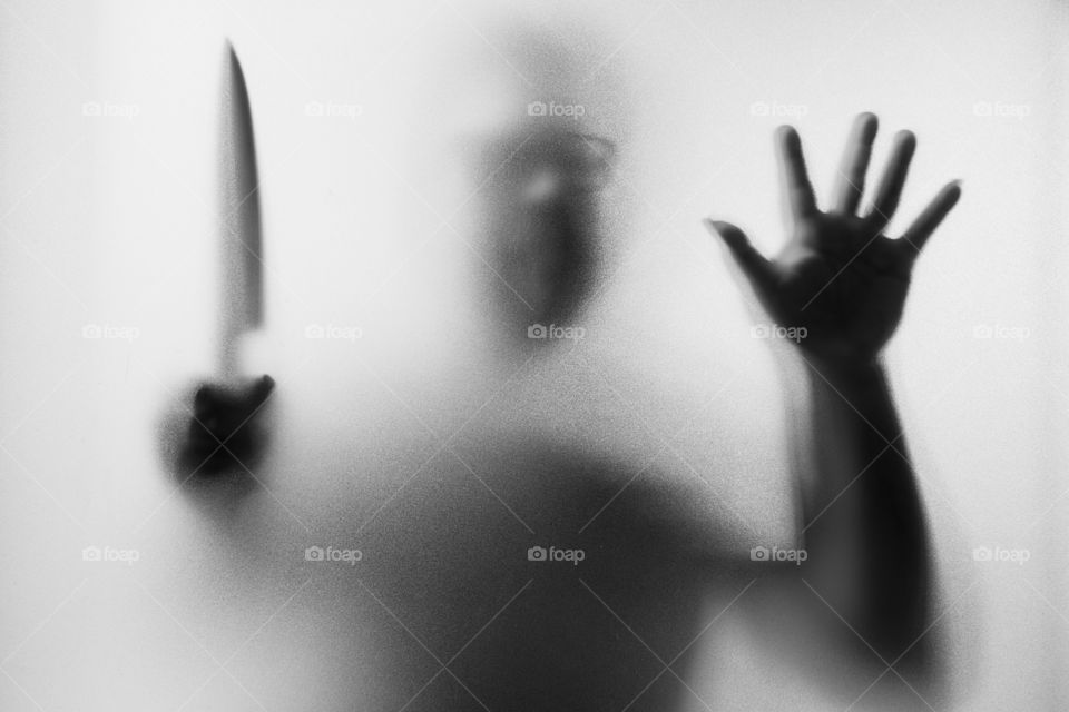 Horror Murderer. Dangerous man behind the frosted glass with a knife on his hand.Halloween background.Black and white picture