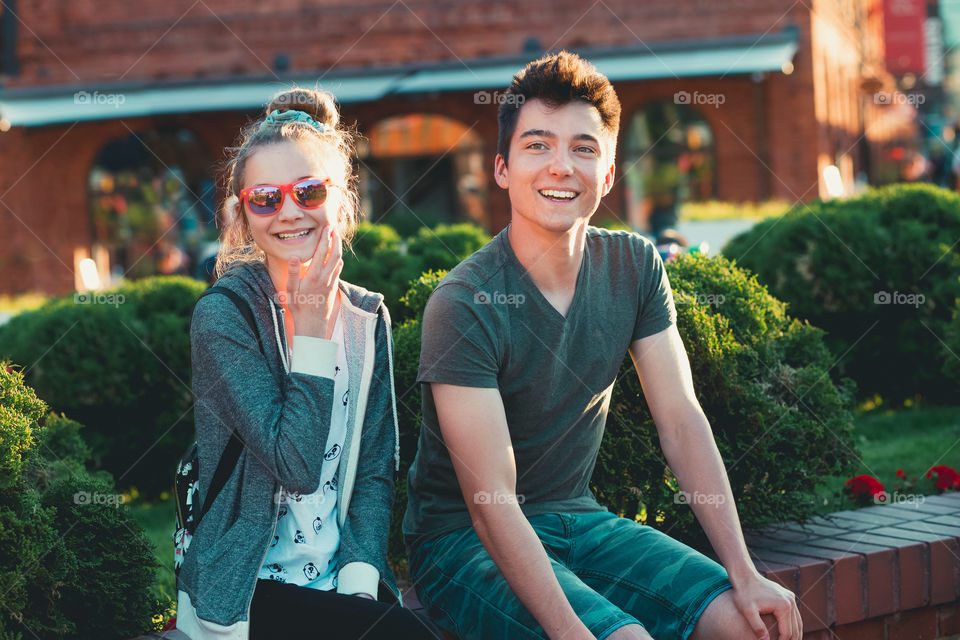 Couple of friends, teenage girl and boy,  having fun together, sitting in center of town, spending time together