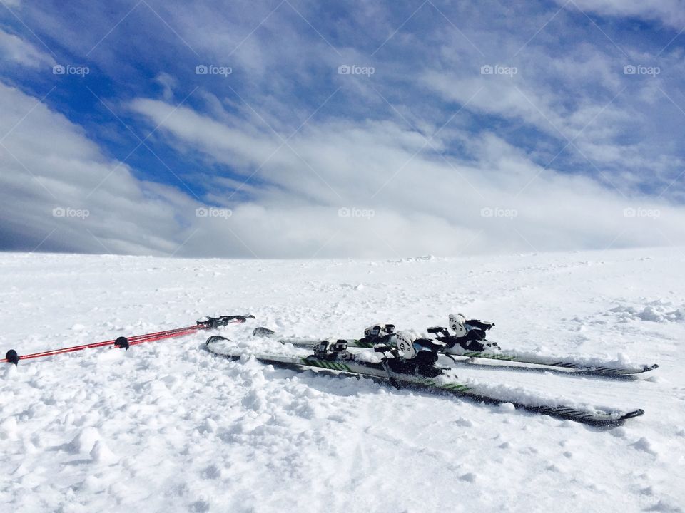 Skis and ski poles on the snow with blue sky in the background
