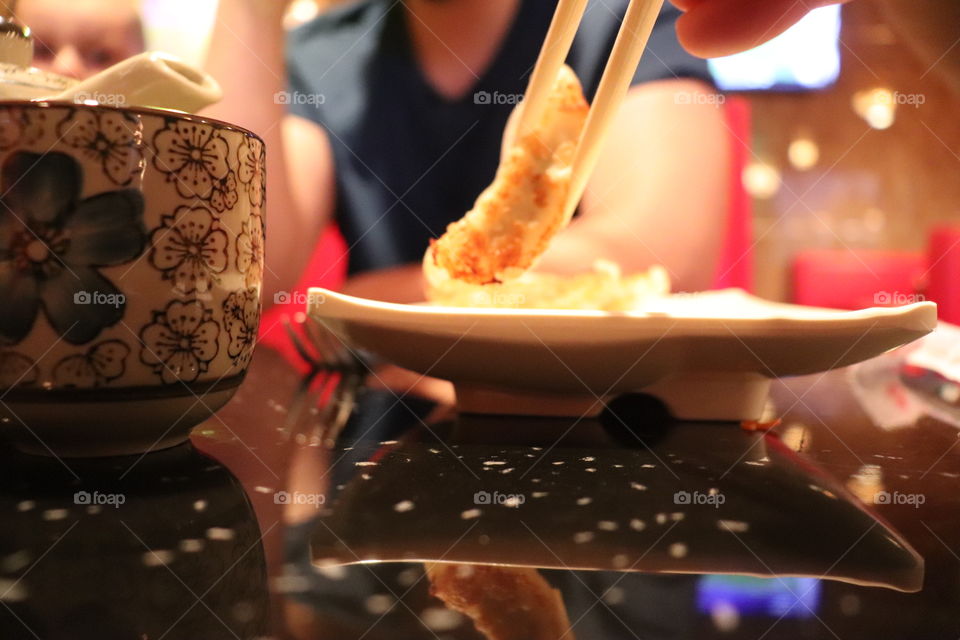 Close up of a dumping or gyoza being picked up with chopsticks with a blurred man in the background. 